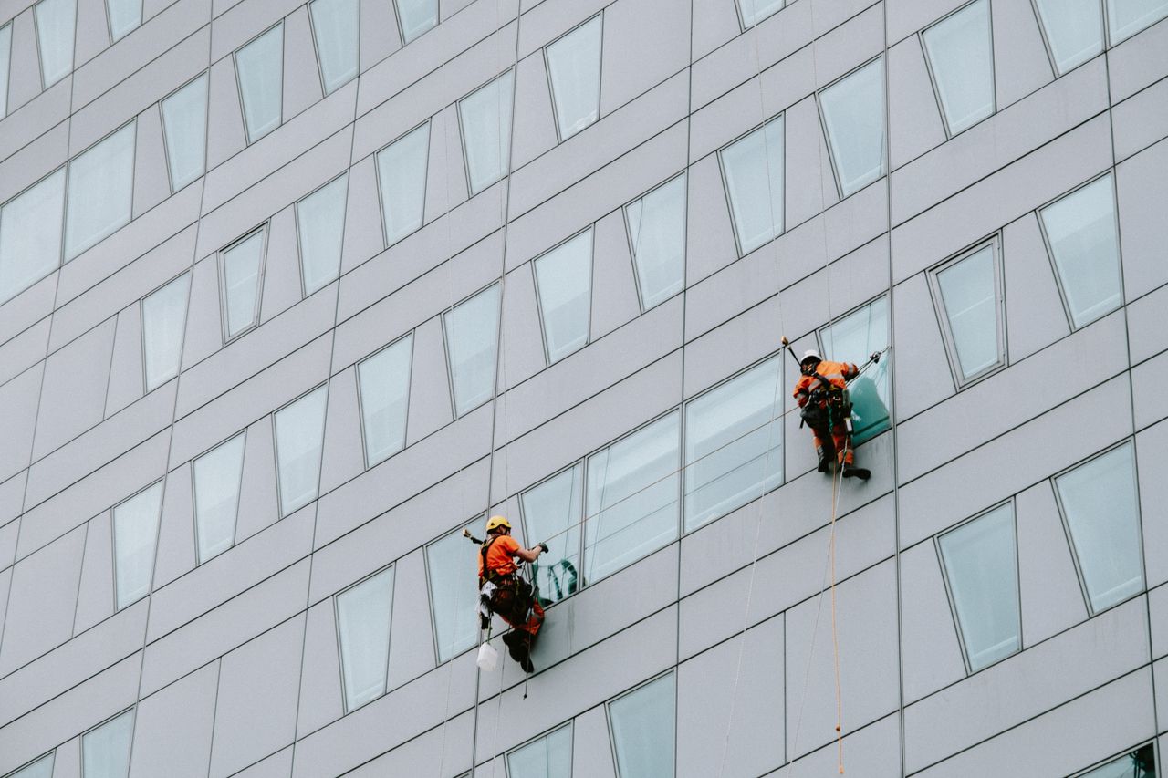 Des laveurs de vitres en hauteur, équipés de matériel de sécurité, nettoient la façade d’un gratte-ciel.